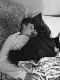 a man and woman sleeping on a bed next to each other in black and white