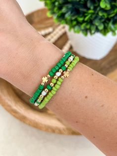 a woman's arm wearing green and gold beaded bracelets with flowers on them