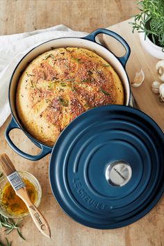 a blue casserole dish sitting on top of a wooden table next to garlic