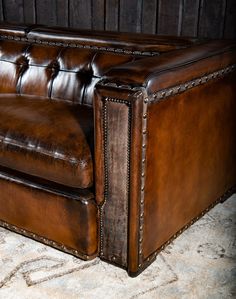 a brown leather couch sitting on top of a carpeted floor next to a wooden wall