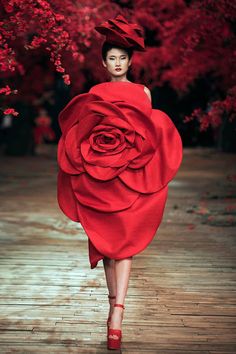 a woman is walking down the runway in a red dress with a rose on it