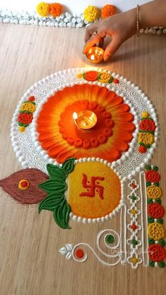 a woman is decorating the floor with colorful flowers and leaves on it, while holding a lit candle in her hand