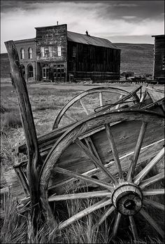 an old wooden wagon sitting in front of a building with two barns on the other side