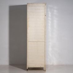 a tall white wooden cabinet sitting on top of a floor next to a gray wall