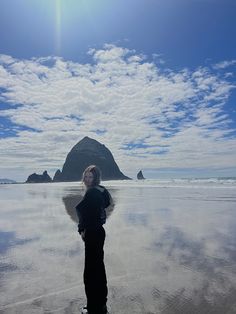 a woman standing on top of a sandy beach under a blue sky with white clouds