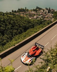 an orange and white race car driving down a road next to the ocean with trees on both sides