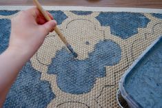 a person holding a pencil in their hand near a rug with blue flowers on it