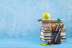 an apple sitting on top of a pile of books next to pencils and markers