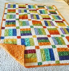 a multicolored quilt is laying on top of a white bedspread with an orange edge