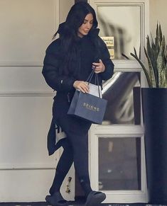 a woman in black coat and leggings carrying shopping bags while walking out of a door