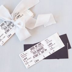 two tickets tied together with a white bow on top of each other and some black paper