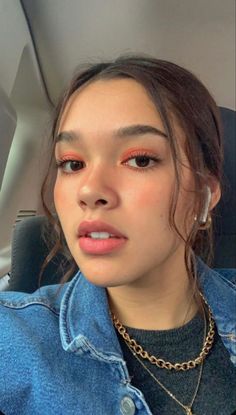 a young woman wearing a denim jacket and gold necklace, sitting in the back seat of a car