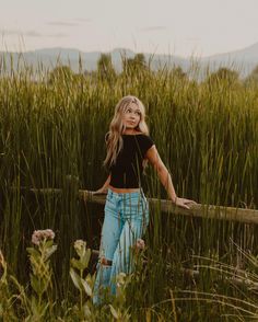 a woman standing in tall grass next to a wooden fence