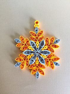 an origami snowflake made out of paper on a white surface with blue and yellow accents