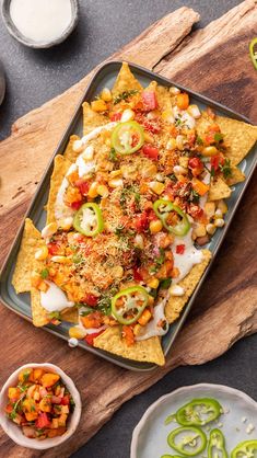 nachos on a tray with salsa and sour cream in the background, along with other dishes