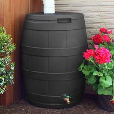 a black barrel next to some flowers and a water faucet on the side of a building