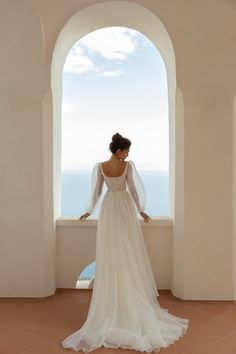 a woman in a wedding dress looking out an arched window at the ocean and sky