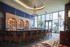 a bar with lots of chairs around it in front of a large window and potted plants