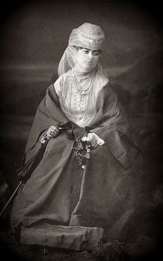 an old fashion photo of a woman wearing a veil and holding a cane in her hand