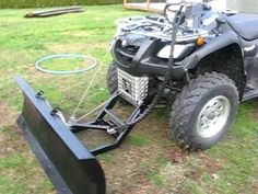 a black four - wheeler parked in the grass with a snow plow attached to it