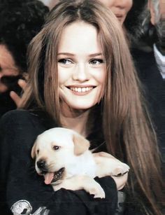 a woman holding a puppy in her arms and smiling at the camera with other people behind her