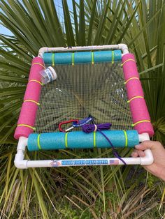 a person holding up a pink and blue net with scissors on it in front of some palm trees