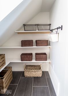 an attic bathroom with white shelving and baskets on the shelves, black tile flooring