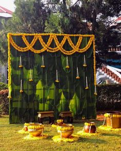 an outdoor stage set up with yellow flowers and hanging decorations on the wall, surrounded by green grass