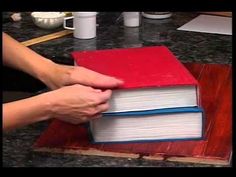 a person holding a red book on top of a wooden table