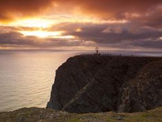 the sun is setting over an ocean cliff