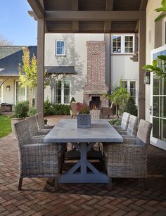 an outdoor dining table with chairs and a fireplace in the back yard, surrounded by brick pavers