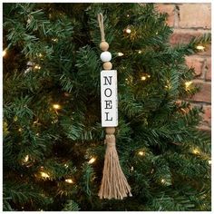 a christmas tree with a sign that says noel hanging from it's side and a tassel on the top