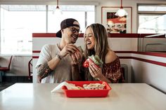 a man and woman sitting at a table with food in front of them, smiling