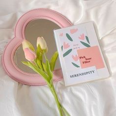 a pink heart shaped mirror sitting on top of a white bed next to a flower