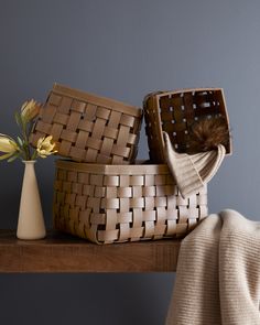 two woven baskets sitting on top of a wooden table next to a vase with flowers