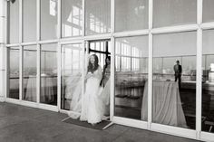 a woman in a wedding dress walking out of a building with her veil blowing in the wind