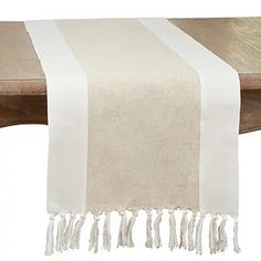 a white table runner with tassels on the edge and a wooden bench in the background