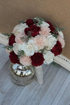 a bridal bouquet with red and white flowers in a silver vase on the floor