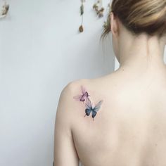 a woman with a butterfly tattoo on her upper back shoulder and behind her is a white wall