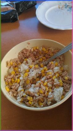 a bowl filled with rice, corn and meat on top of a wooden table next to a plate