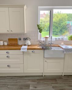 a kitchen with white cabinets and wooden counter tops, along with a window that looks out onto the yard