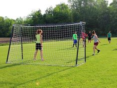 a group of young people playing soccer on a green field with trees in the background