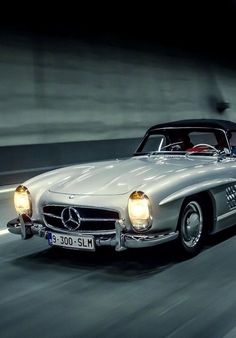 a mercedes 300 sl roadster driving on a road at night with the headlights on