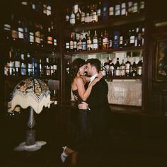 a man and woman kissing in front of a bar with liquor bottles on the shelves