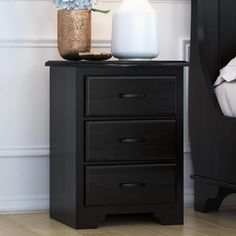 a black night stand with three drawers and a vase on top