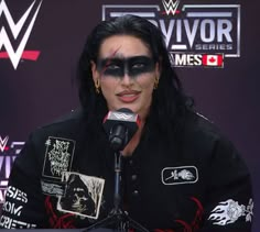 a woman with black makeup and face paint on her face is speaking into a microphone