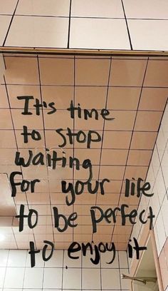 graffiti on the ceiling of a bathroom stall saying it's time to stop waiting for your life to be perfect to enjoy it