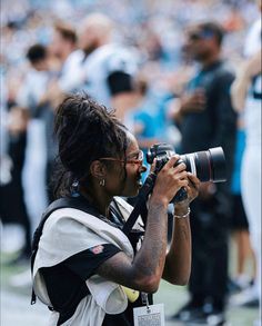 a woman taking a photo with her camera on the field at a football game in front of a large crowd