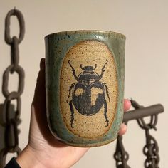 a hand holding a coffee cup with a bug on it