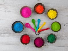 colorful powder in small bowls with spoons on white wooden table, top view from above